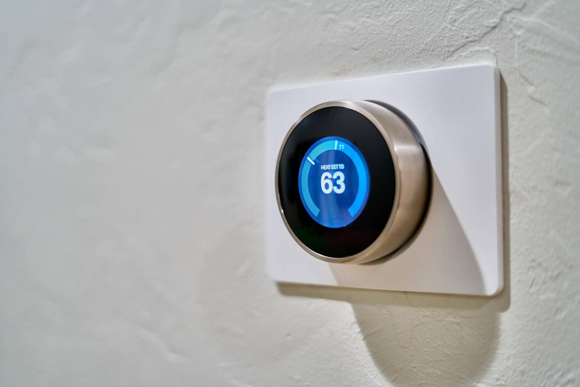 A smart thermostat on a white wall showing 63